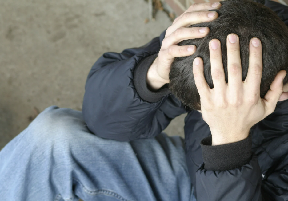 Person sitzt zusammengekauert und hält sich mit beiden Händen den Kopf