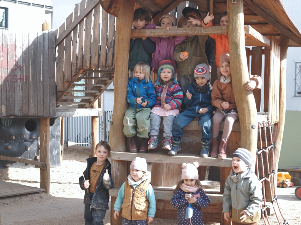 Kindergruppe auf einem Holzspielplatz vor und in einer Spielhütte.