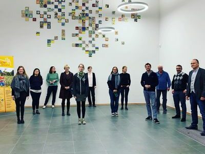 Personengruppe in einer Ausstellungshalle unter einer Wandinstallation aus vielen kleinen Bildern