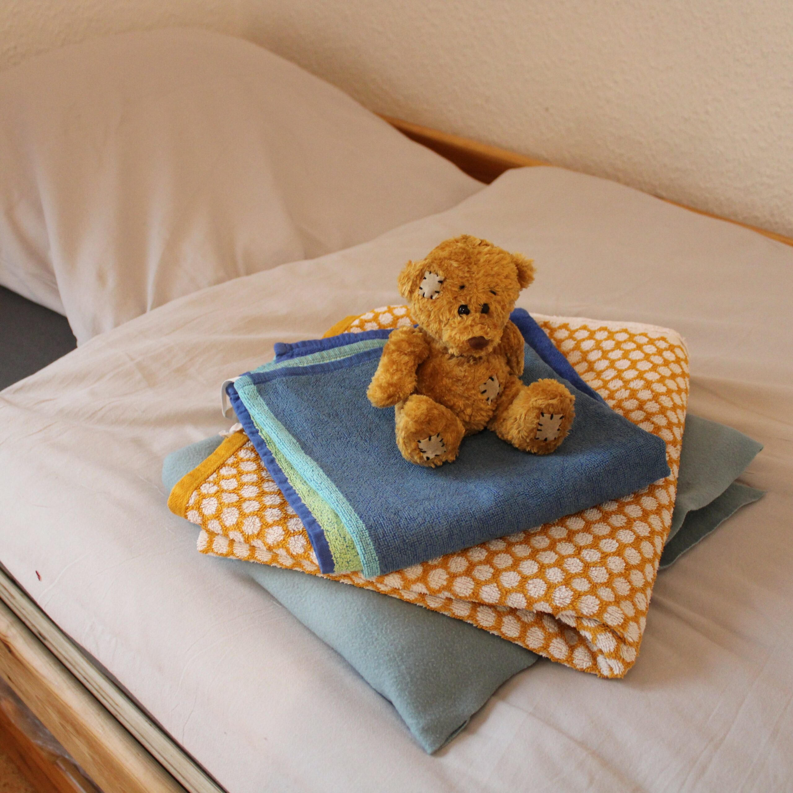 Brauner Teddybär sitzt auf einem Stapel gefalteter Handtücher auf einem Bett
