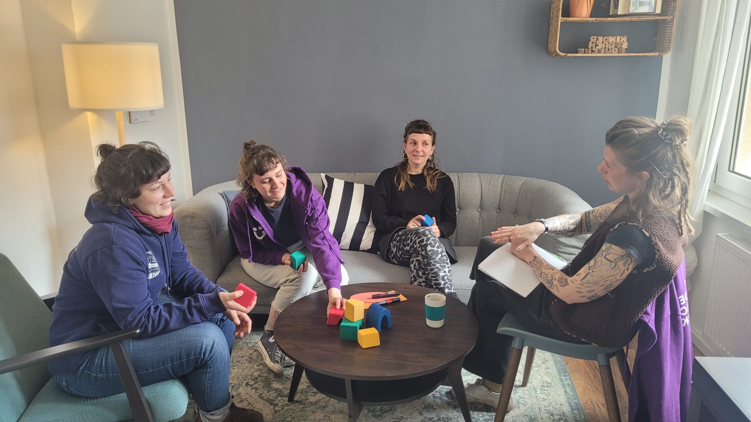 Vier Personen sitzen um einen Couchtisch mit bunten Bauklötzen und unterhalten sich