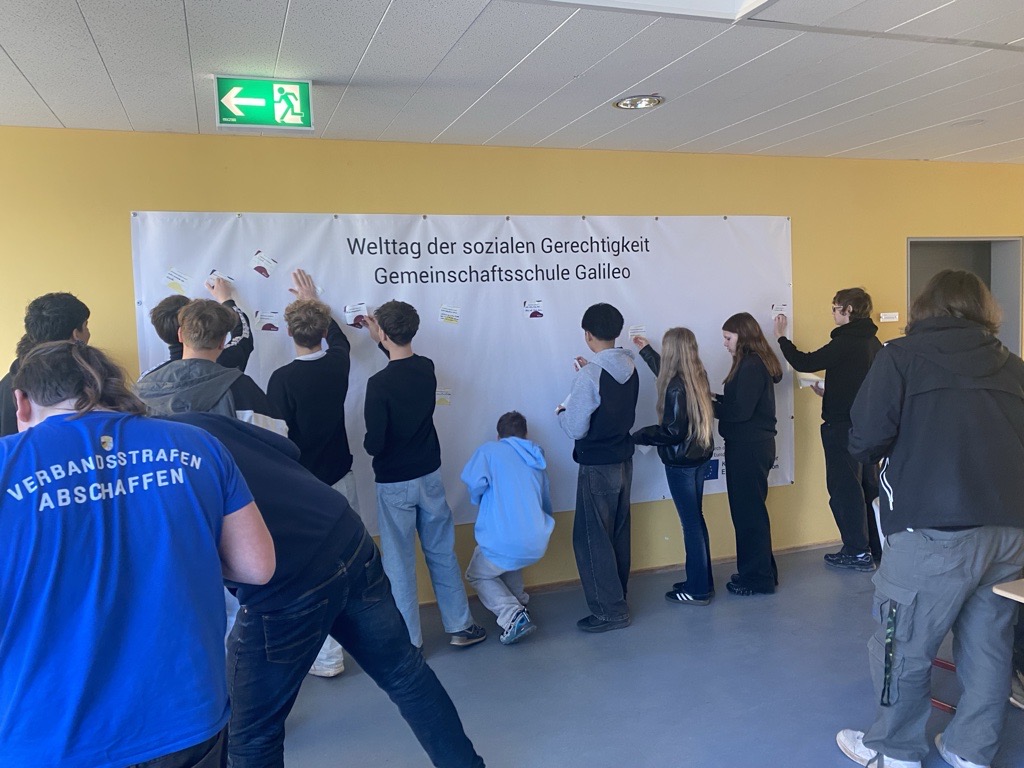 Jugendliche hängen Karten an ein Banner zum Welttag der sozialen Gerechtigkeit an der Gemeinschaftsschule Galileo