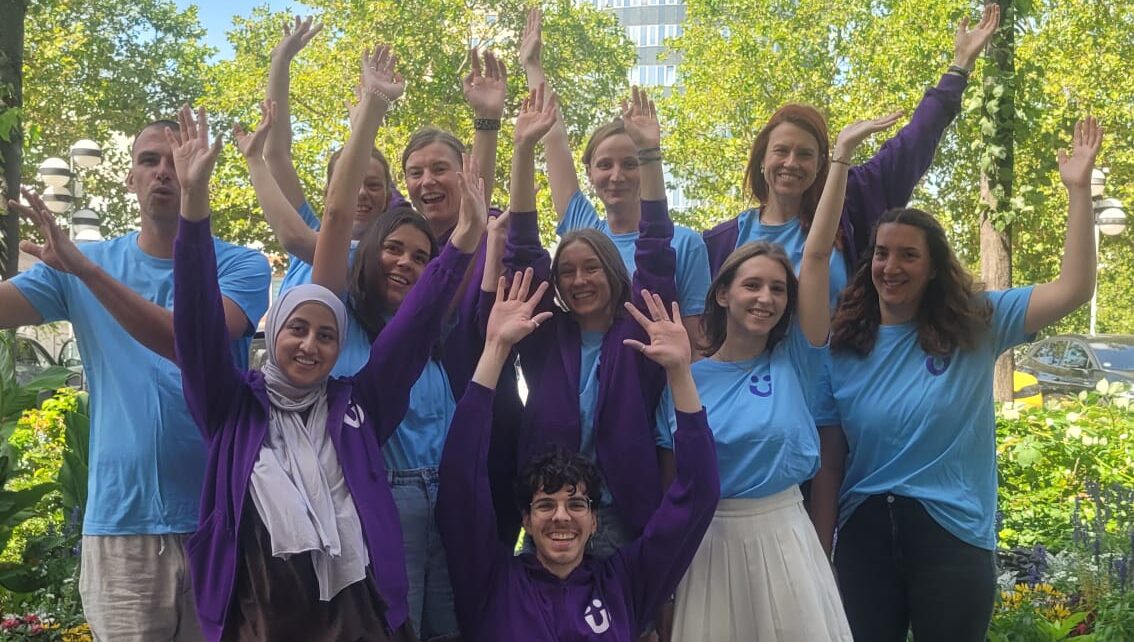 Gruppe von Menschen in blauen und violetten Shirts jubelt mit erhobenen Händen im Freien