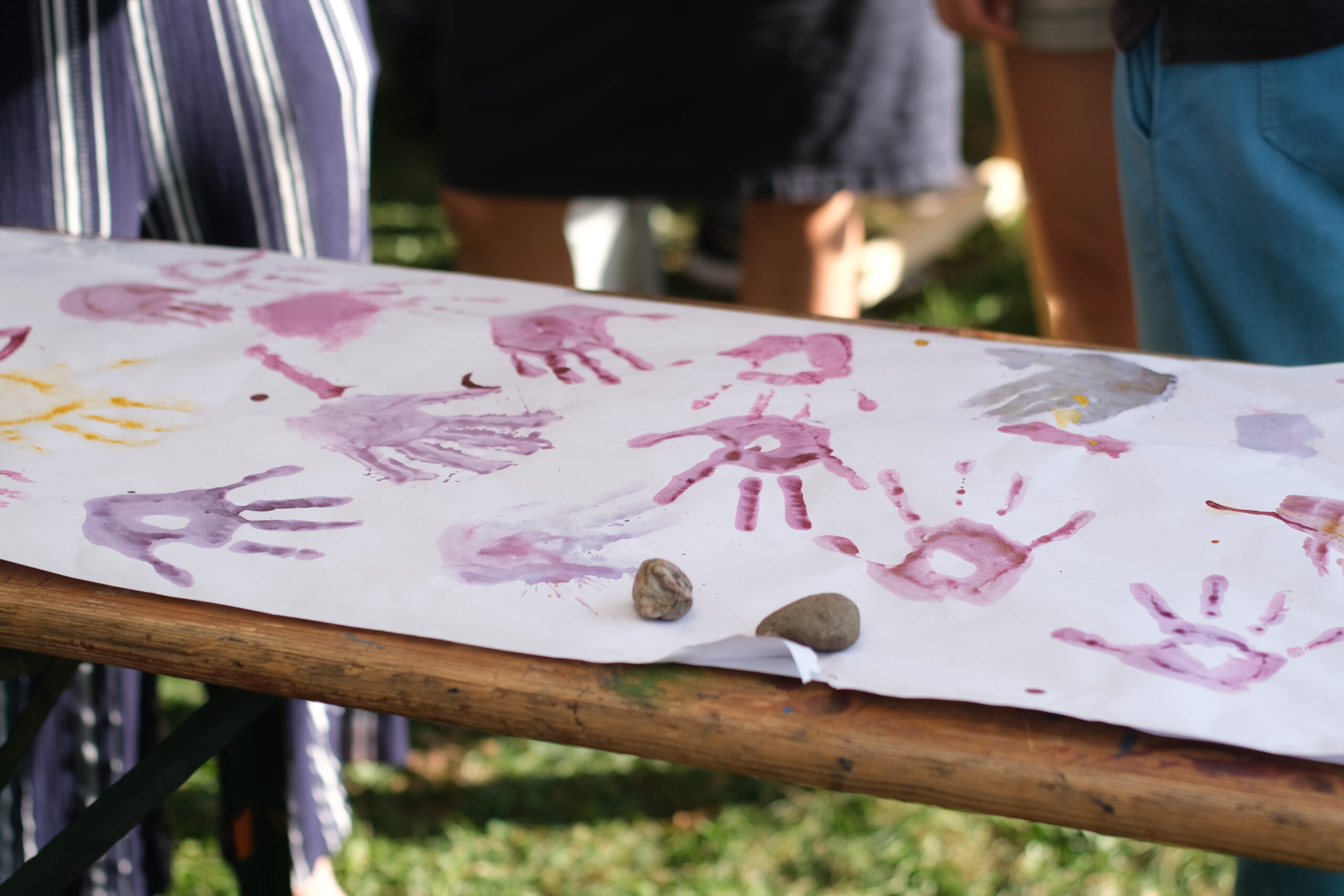 Verschiedenfarbige Handabdrücke in Rosa, Lila und Gelb auf weißem Papier, das auf einem Holztisch liegt