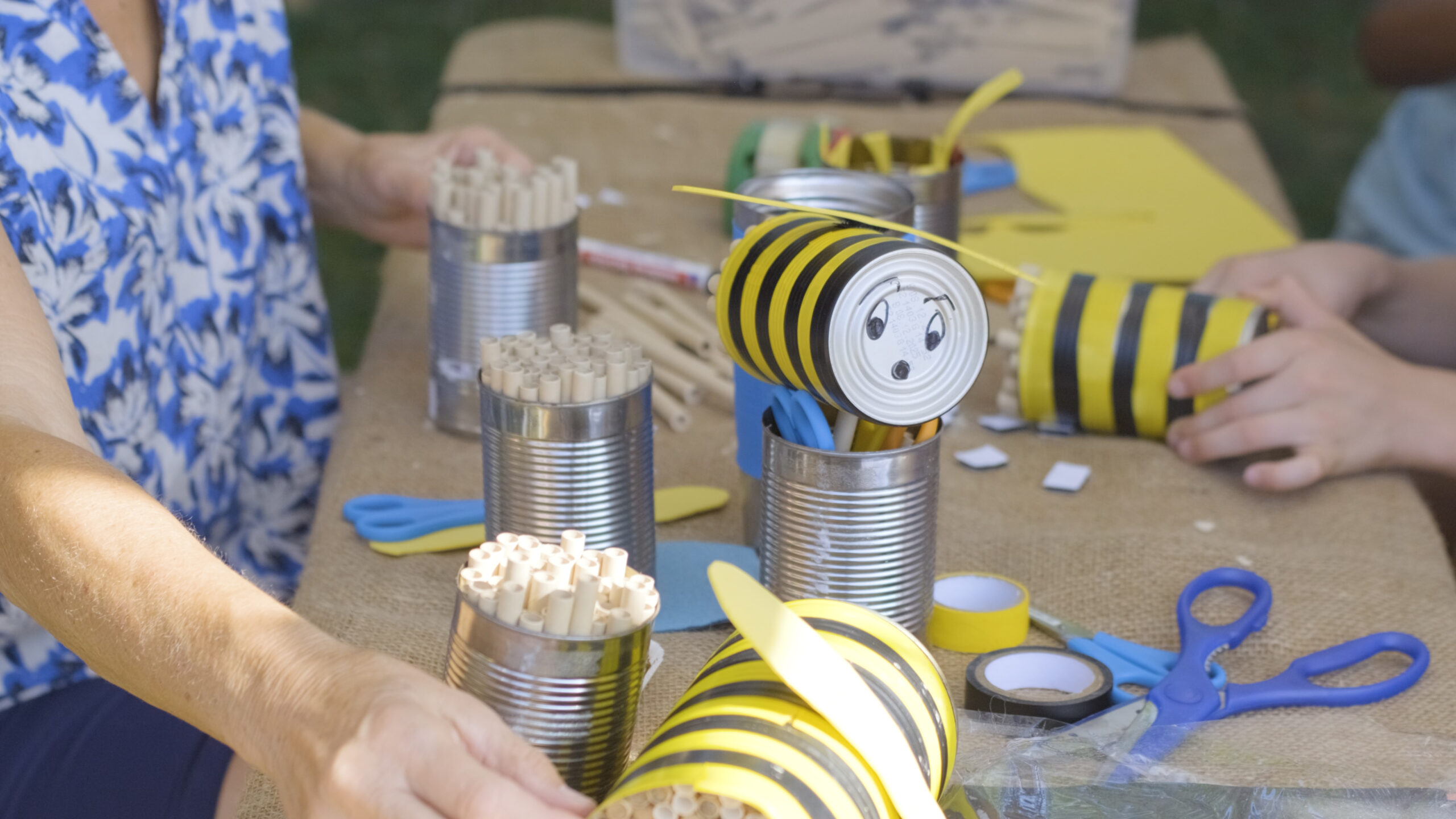 Bastelrunde: Aus Konservendosen gebastelte Bienen mit gelb-schwarzen Streifen, Augen und Flügeln auf einem Tisch
