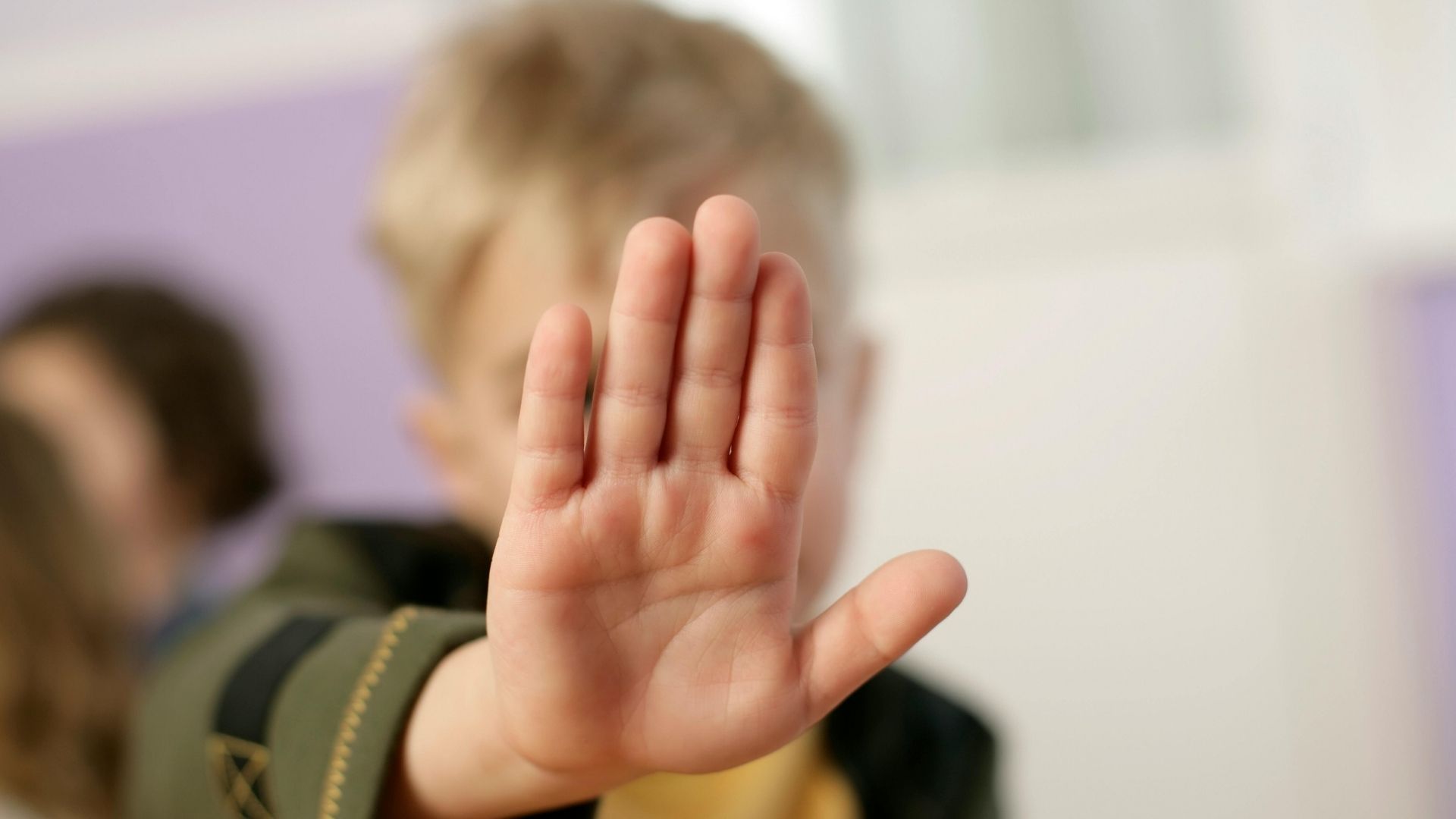 Ein Kind streckt abwehrend die Hand mit der Handfläche nach vorn, dahinter unscharf weitere Kinder