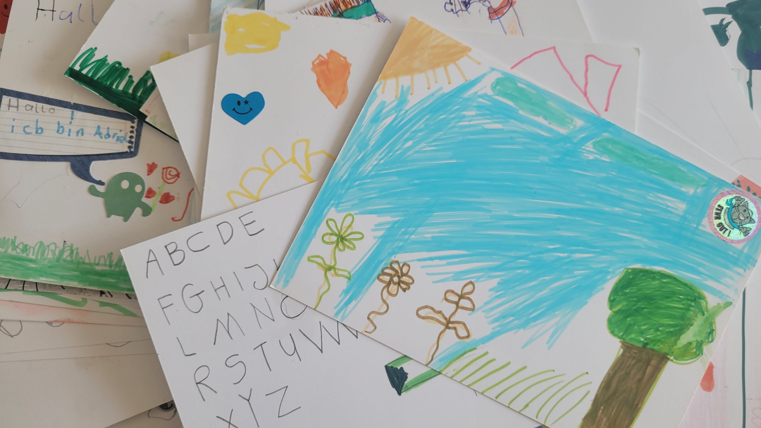 Bunte Kinderzeichnungen: Sprechblase mit Schriftzug, Alphabettabelle, Sonne, Blumen und Baum