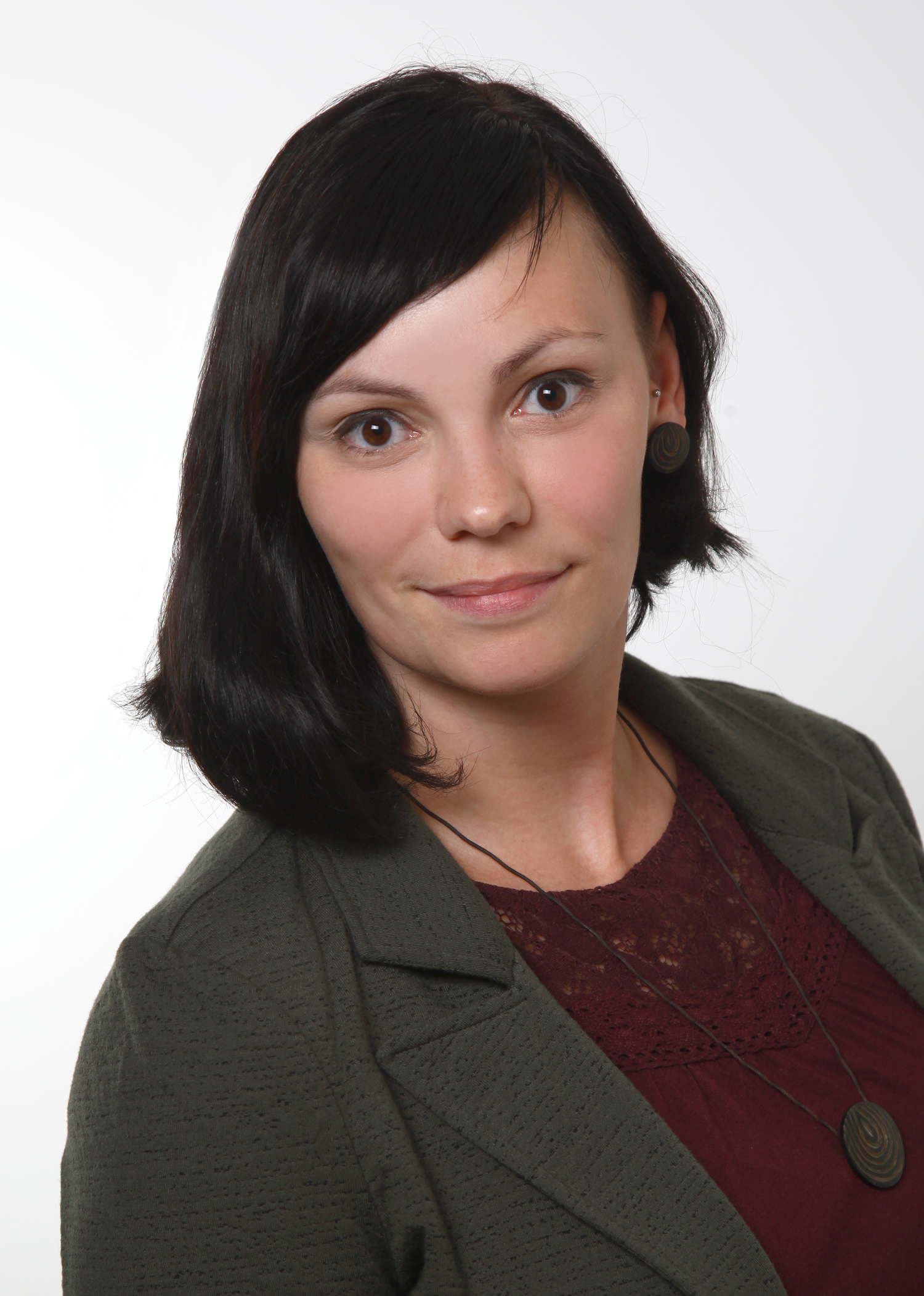 Porträt einer lächelnden Frau mit dunklen Haaren, grünem Blazer und weinrotem Top