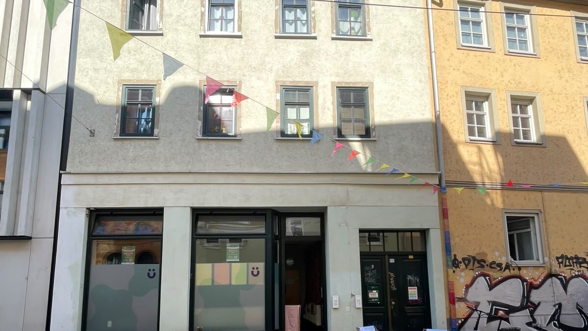 Straßenansicht einer Hausfassade mit Ladenlokal, bunten Wimpeln und pastellfarben beklebten Schaufenstern