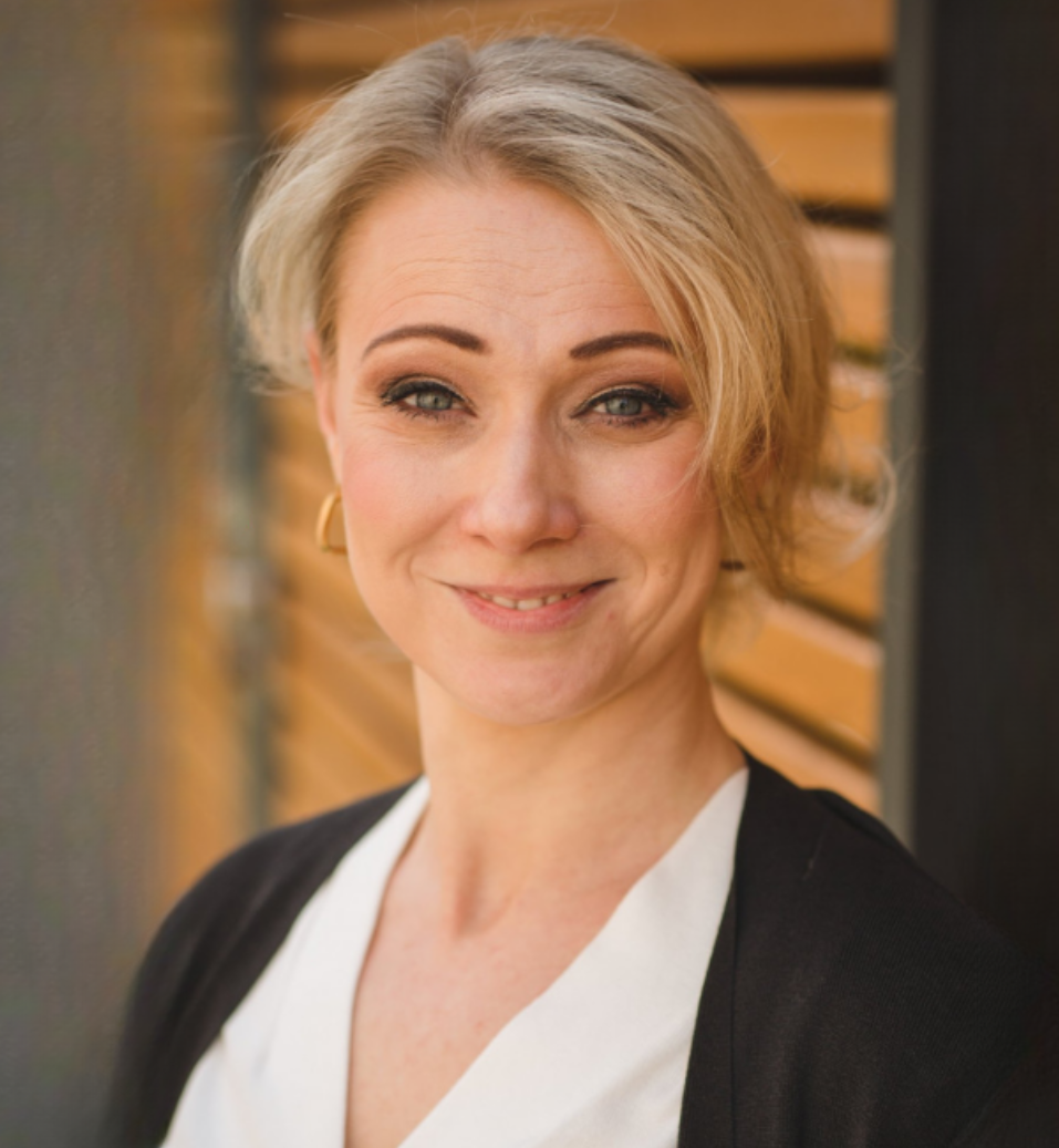 Porträt einer lächelnden blonden Frau in schwarzer Jacke über weißer Bluse